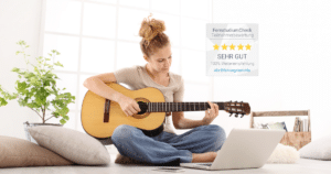 Akustikgitarre online lernen. Frau lernt Akustikgitarre online im Wohnzimmer mit Laptop – Blues, Rock & Folk Gitarrenkurs der New Music Academy.